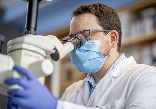Person in glasses and lab wear operating microscope.