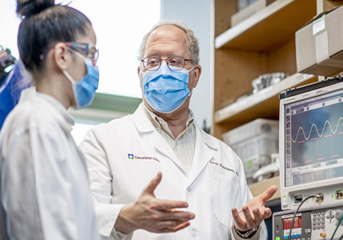 Two people with lab coats talking in front of research equipment.
